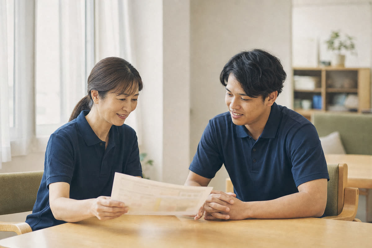 介護施設の休憩室で、外国人スタッフと日本人の担当者が母国語の資料を見ながら面談する様子